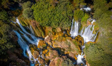 Kirlenmemiş doğada küçük bir şelalenin havadan görünüşü. Su, kayalar ve ağaçlar doğal bir manzarada.
