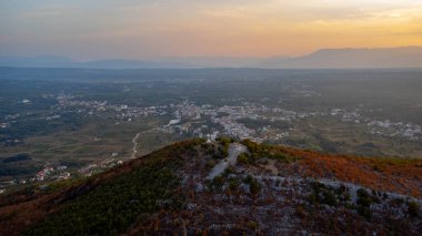 Top of Krievac mountain with white cross. Background of tourist town of Medjugorje, Bosnia and Herzegovina. Aerial view of panorama at sunrise. clipart