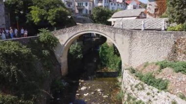 İnsansız hava aracından görünen eğri köprü. Bosna-Hersek 'in Mostar kentinin sokaklarında küçük bir köprü. Doğayla ve evlerle çevrili karakteristik köprü.