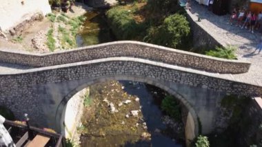İnsansız hava aracından görünen eğri köprü. Bosna-Hersek 'in Mostar kentinin sokaklarında küçük bir köprü. Doğayla ve evlerle çevrili karakteristik köprü.