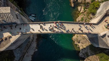 Mostar 'daki eski köprünün aşağı manzarası. Neretva Nehri 'nin havadan görünüşü ve turistlerin geçtiği ünlü köprü.