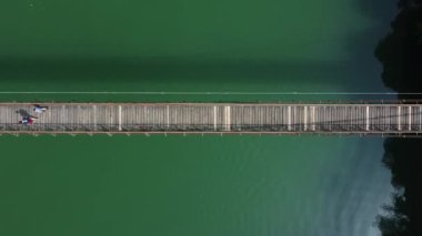 Dar bir yaya köprüsünde yeşil suyla yürüyen iki insanın en tepeden görünen görüntüsü. İtalya 'daki Arsi Gölü' nde doğal hava manzarası