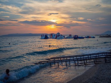 Hırvatistan 'da gün batımı, Dalmaçya kıyısındaki Makarska plajında. Güneş 'in muhteşem manzarası ve akşam renkleri. Suda şişirilebilir oyunlar.