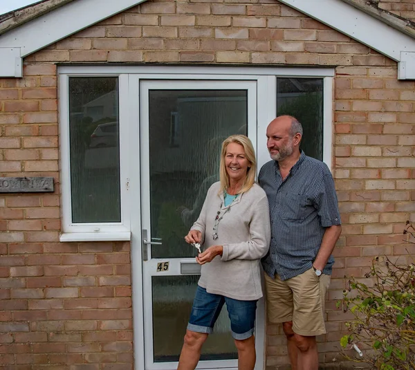 New home buyers are given the keys to their new home from the estate agent. They stand at the doorstep soon to move into the residential property. Property sales and rental.