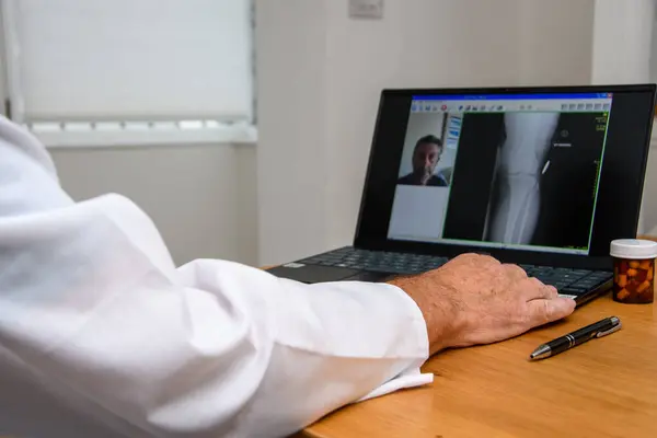 Online GP Doctor\'s appointment. Consultant working on laptop. Xray of a patient on computer screen whilst in remote chat with DR in hospital or clinic. Focus on keyboard.