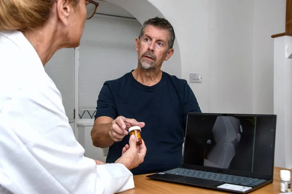 Doktor randevusundaki hastaya pratisyen hekim tarafından bir kap hap veriliyor. Hastanın dizinin röntgeni klinikte danışmanlık yaparken bilgisayar ekranında incelenir..