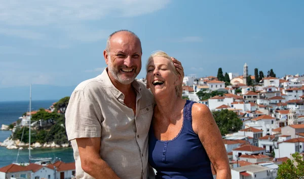 Happy couple laughing whilst holidaying. Relaxed, fun, sunny capture of a middle aged man and woman sharing a joke with a backdrop of terracotta roofed white washed houses.