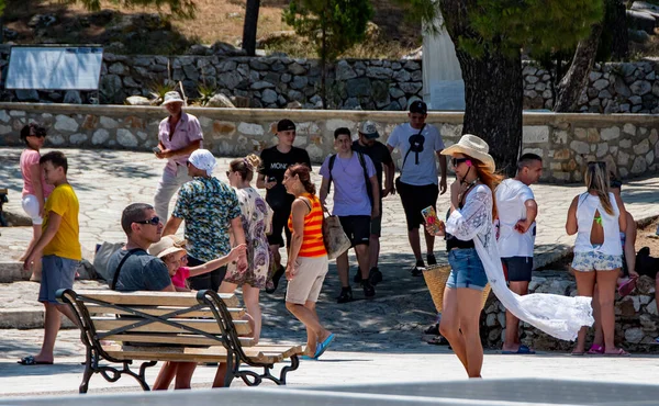 Skiathos Yunanistan. 07-05-23 Turist Bourtzi boyunca sarong 'la yürüyor. İnsanlar sıcak bir yaz gününde ağaçların gölgesinde oturdular. Yoğun bir tatil, tatil sahnesi. Boşluğu kopyala