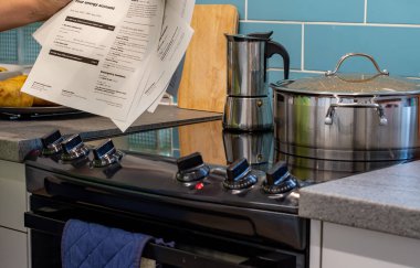 Devon UK. 09-24-23. Artan enerji faturaları, ödenecek ödemeleri gösteren kağıt beyannameler. Mutfak arka planında elektrikli fırın, hob.