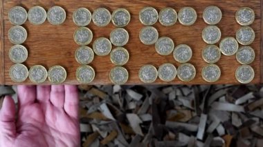 Exeter İngiltere. 11-14-23. Nakit ve finansal para imajı. CASH kelimesi bir masadan alınıp bir insanın eline konulan bozuk paralardan yapılmıştır. İngiliz para birimi ve bankacılık veya tasarruf kavramı.  