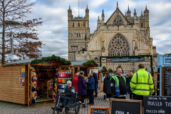 Exeter İngiltere. 11-28-23. Exeter Noel pazarında müşteriler. İnsanlar Noel Pazarı 'nda yürürken market tezgahlarına hayran kalır, yiyecek, hediye ve oyuncak alırlar. Kış boyunca aydınlatılmış dekorasyonlar.