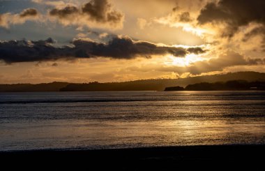 Gün batımı sahnesi, insanlar altın gün ışığında parıldayan bir denize karşı siluetlendi. Aileler ve plaja gidenler dramatik bir gökyüzü ile akşam üstü gün ışığında yürüdüler..