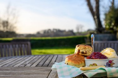Kremalı çay, çörekler, reçel ve pıhtılaşmış krema kırsal manzaralı bir bahçe masasına konmuş. Öğleden sonra İngiliz çayı. Fotokopi alanı. Çimenli masaya odaklan, bokeh arkaplan.
