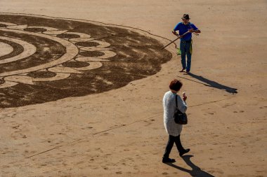 Torquay, Devon uk. 09-17-24. Beach art at Torquay in Devon. Artist carves a mandala wheel in the sand for tourist attraction. Buddhism design promoting spirituality and meditation. clipart