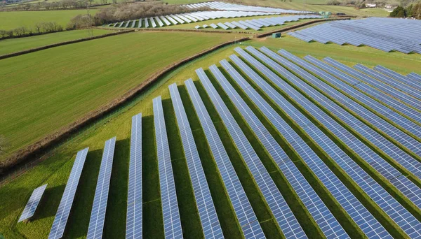Solar panel farm aerial view with good copy space. Fields full of solar panels sit in green grassy fields producing clean zero carbon energy. Solar energy production. sustainable climate visuals.