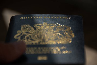 Weston Super Mare, N. Somerset, İngiltere. 10-03-23. İngiliz pasaportu gösterişsiz. İngiliz pasaportu kelimelerine özenle odaklanmış karanlık ve kasvetli bir görüntü. Pasaport boyunca bir ışık şeridi var..