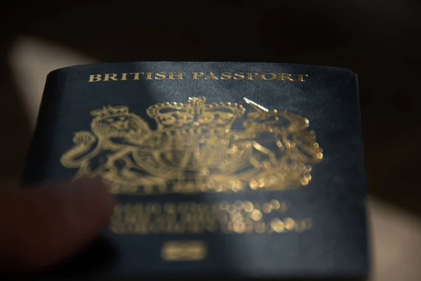 Weston Super Mare, N. Somerset, İngiltere. 10-03-23. İngiliz pasaportu gösterişsiz. İngiliz pasaportu kelimelerine özenle odaklanmış karanlık ve kasvetli bir görüntü. Pasaport boyunca bir ışık şeridi var..