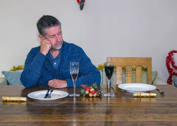 Loneliness at Christmas image. A lonely man sits at a Christmas table with an empty plate by his side where someone significant would have been. Loss and solitude image. Selective focus on his face