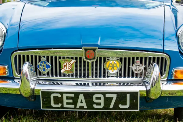 Exmouth, Devon, İngiltere. 08-13-23. MGB klasik mavi renkli GT araba. Krom ön ızgaranın, klasik rozet sergilenen resmini kapat. MG rozetine odaklan.