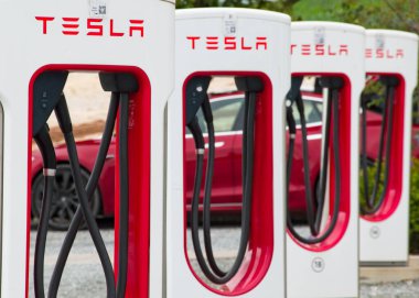 Exeter, Devon, İngiltere. 08-08-23. Tesla EV arkasında kırmızı bir Tesla olan bir kuyrukta şarj istasyonları. İlk şarj istasyonuna seçici odaklan. 