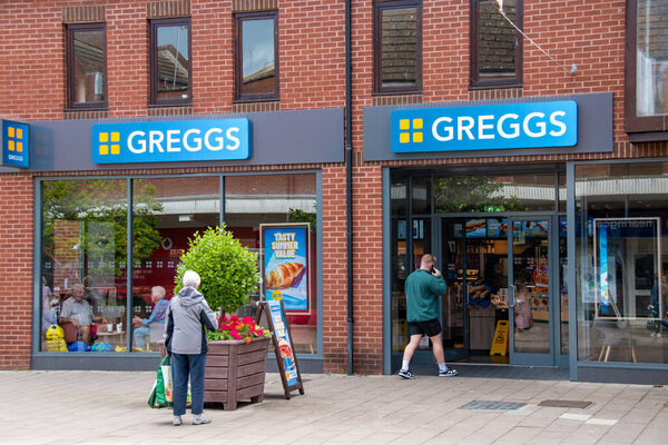 Exmouth, Devon, uk. 08-12-23. Greggs bakery on a high street. A customer walks into the store. Selective focus on the Greggs sign above the door. Hot beverage and cafe image with copy space.