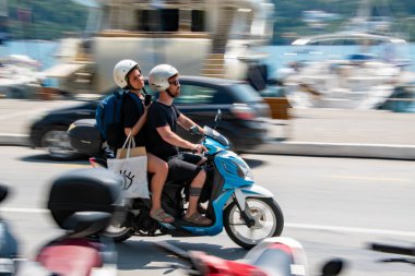 Skiathos, Yunanistan. 07-02-2023. Yunanistan 'ın Skiathos kentindeki sahil şeridi boyunca bir scooter zumluyor. Skiathos motosiklet kiraladı. Resimde hareket bulanıklığı olan ama odak motorlu resim döndürme.