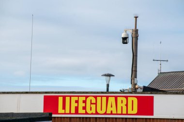 Exmouth, Devon, İngiltere. 26 Ocak 2023. Büyük cankurtaran işareti kırmızı ve sarı. Arka planda bir CCTV kamerası sahile bakıyor. İşaretlere odaklan. Uzayı kopyala Yazı.