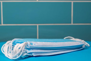 Mavi fayanslı mavi bir zeminde duran mavi yüzlü maskeler. Uzayı kopyala. Üst maskenin sol kenarına seçici odaklanma. Beyaz kayışlı yeni maskeler almaya hazır.