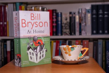 Churston, Devon, İngiltere. 14 Aralık 2022. Bill Bryson 'ın Evdeki Kitabı. Ön kapağın ortasındaki Bryson 'daki Y' ye odaklan. Kitabın yanındaki masada bir çay fincanı oturuyor..