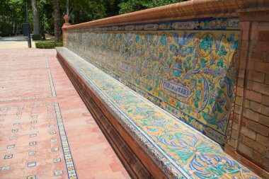 Sevilla, İspanya. 8 Haziran 2022. İspanya 'da Seville' de halka açık bir parkta renkli, süslü bir bank. Yumuşak bir arka planı olan keskin odaklı ön plan. Mavi sarı ve yeşil desenli fayanslar..