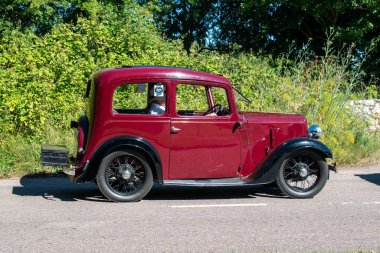 Powderham, Devon, İngiltere. 9 Temmuz 2022. Austin Yedi Ruby klasik arabası, siyah ve koyu kırmızı, tel tekerlekleri olan küçük, arsız, tarihi bir araç. Bir yaz günü köy yolunda araba sürerken resmedilmiş..