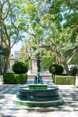 Cadiz, İspanya. 3 Haziran 2022. Cadiz Genoves Parkı. Çeşmenin üzerinde bir ağaç dalının kıvrıldığı sakin bir sahne. Benekli ışık yeşilin tonlarını vurgular. 