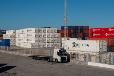 Cadiz, İspanya. 22 Mayıs 2022. Nakliye konteynırları rıhtımda düzgünce istiflenmiş. Arka planda beyaz nakliye konteynırları olan beyaz bir kamyon..