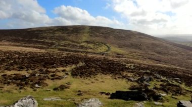 Grimspound bronz çağ köyü ve Hookney Tor, Dartmoor, Camera manzarayı tarıyor. Dartmoor Ulusal Parkı 'nda. Mavi gökyüzü, beyaz bulutlar ve kara bulutlar arazide hareket ediyor..