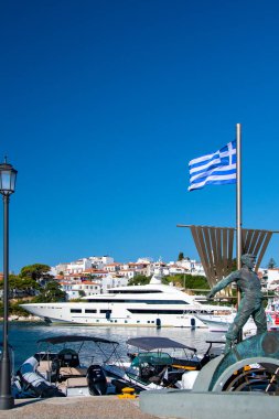 Skiathos, Yunanistan. 06-20-24. Yunan bayrağının arkasında demirli süper yatı olan kaykaylar. Arkaplanı Picturesque Plakes dolduruyor. Renkli tatil resmi. 