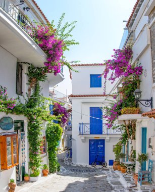 Skiathos, Yunanistan. 06-21-24. Skiathos renkli çiçekler ve mavi kapılarla Yunan beyaz binalarına karşı antika beyaz cadde. 