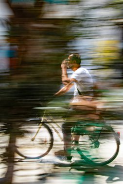 Skiathos, Yunanistan. 06-21-24. Tek elle hareket eden bisikletçi renkli bir ortamda bulanıklaşıyor.. 