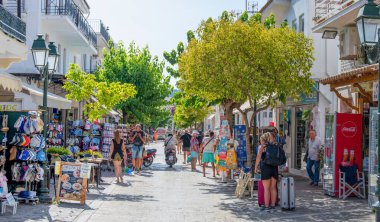 Skiathos, Yunanistan. 06-29-24. Skiathos Panorama filmi Papadiamanti caddesini turistler, renkli dükkanlar ve kafelerle gösteriyor..