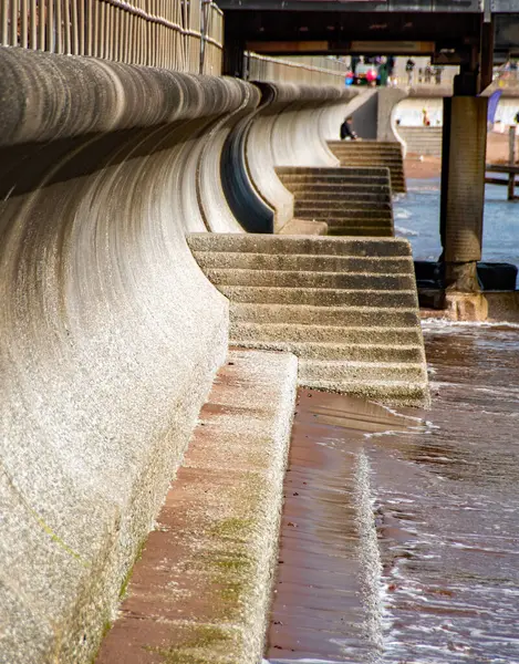 stock image Curved concrete sea wall with concrete steps in foreground. Civil engineering and flood prevention through reinforced coastal sea defenses.