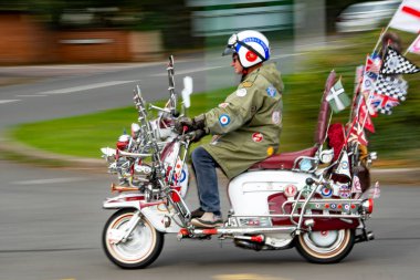 Starcross, Devon, İngiltere. 09-15-24. Mod scooter 'ın arkasında hareket bulanıklığı var. 60 'ların modası vespa lambretta, bir sürü bayrak, rozet ve ayna.. 