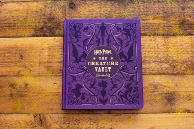 Torbryan, Devon, İngiltere. 10-26-24. Yaratık Kasa Kitabı. Harry Potter. Atmosferik resim, sihirli altın bir çizgi ile tahta bir masa zeminine karşı dizilmiş kitaba götürüyor..