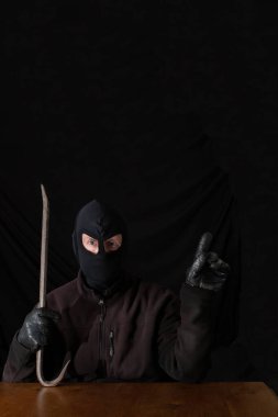 Mesajınız için bir kopyalama alanına işaret ederken Karga Çubuğu tutan maskeli bir hırsızın suç görüntüsü. Siyah arkaplana karşı mükemmel bir fotokopi alanı ile yerleştirilmiş. Suç önleme 