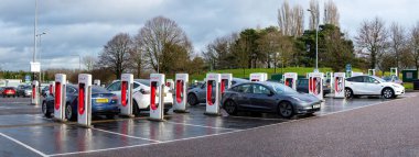 Exeter, Devon, uk. 01-06-25. Wide panoramic picture of Tesla EV's at a charging station. Selective focus on the first charging station. 