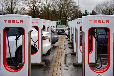 Exeter, Devon, İngiltere. 01-06-25. Tesla EV şarj istasyonları arabaların şarj olduğu bir hatta. İlk şarj istasyonuna seçici odaklan. 