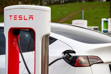 Exeter, Devon, İngiltere. 01-06-25. Bir Tesla EV yakın plan, şarj istasyonunda takılı..