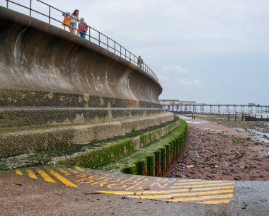 Teignmouth, Devon, İngiltere. 09-15-24. Kıyı aşınması ve inşaat mühendisliği büyük beton bir deniz duvarı. Parlak işaret, ön planda ani bir düşüş olduğunu gösteriyor. Kıyı aşınması ve deniz savunması