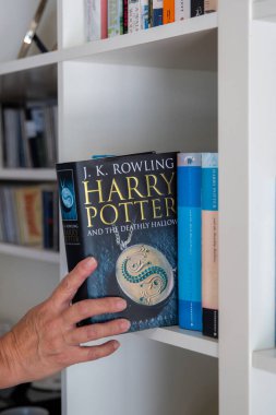 Ideford, Devon, İngiltere. 08-17-24 Harry Potter ve Ölümcül Cadılar Bayramı, yazan J K Rowling. Bir insan eli, beyaz kitap kutusundan kitabı alır. Ön kapağa seçici odaklanma.
