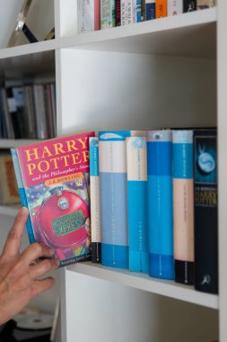 Ideford, Devon, İngiltere. 08-17-24. Harry Potter ve Filozoflar Taşı, yazan J. K. Rowling. Bir insan eli, beyaz kitap kutusundan kitabı alır. Ön kapağa seçici odaklanma.