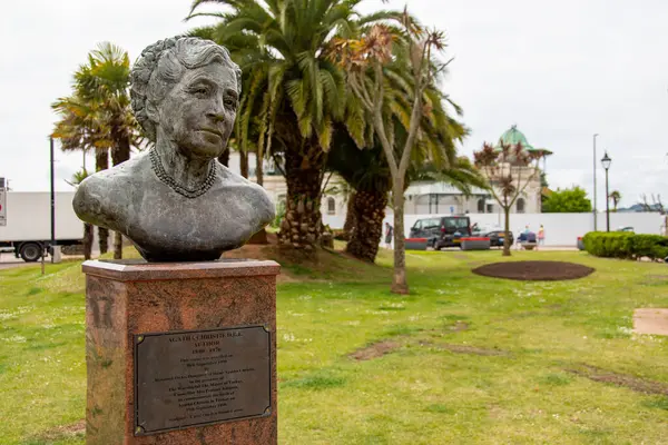 Torquay, Devon, uk. 06-11-25. Agatha Christie 'nin Torquay, Devon' daki büstü. Torquay 'ın ünlü palmiye ağaçları arka planda oturur..
