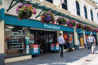 Torquay, Devon, uk. 06-17-25. Poundland indirim mağazası, dışarıda parlak renkli çiçekler var. İngiltere 'nin ana caddesinde tasarruf ve indirim yapan bir pound dükkanı..